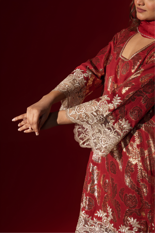 Closeup view of a woman's hand in a maroon ethnic  shimmer kurta set outfit with intricate white embroidery against a vibrant red backdrop.