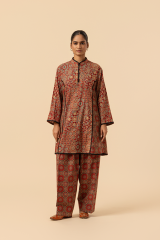 A model showcases a vibrant, patterned ethnic ajrakh printed farshi co-ord set featuring a long tunic and matching pants in rich red tones.