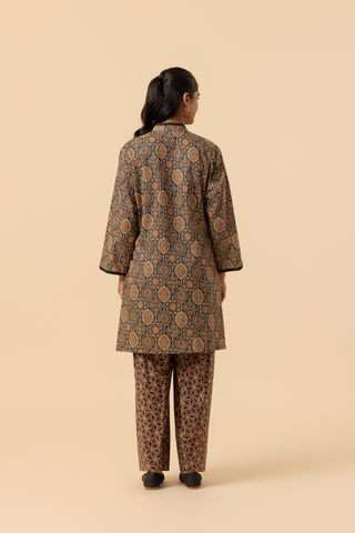 Back view of a model stands in a patterned ajrakh print co-ord set which has brown kurta and matching loose pants against a soft beige background, showcasing traditional ethnic wear.