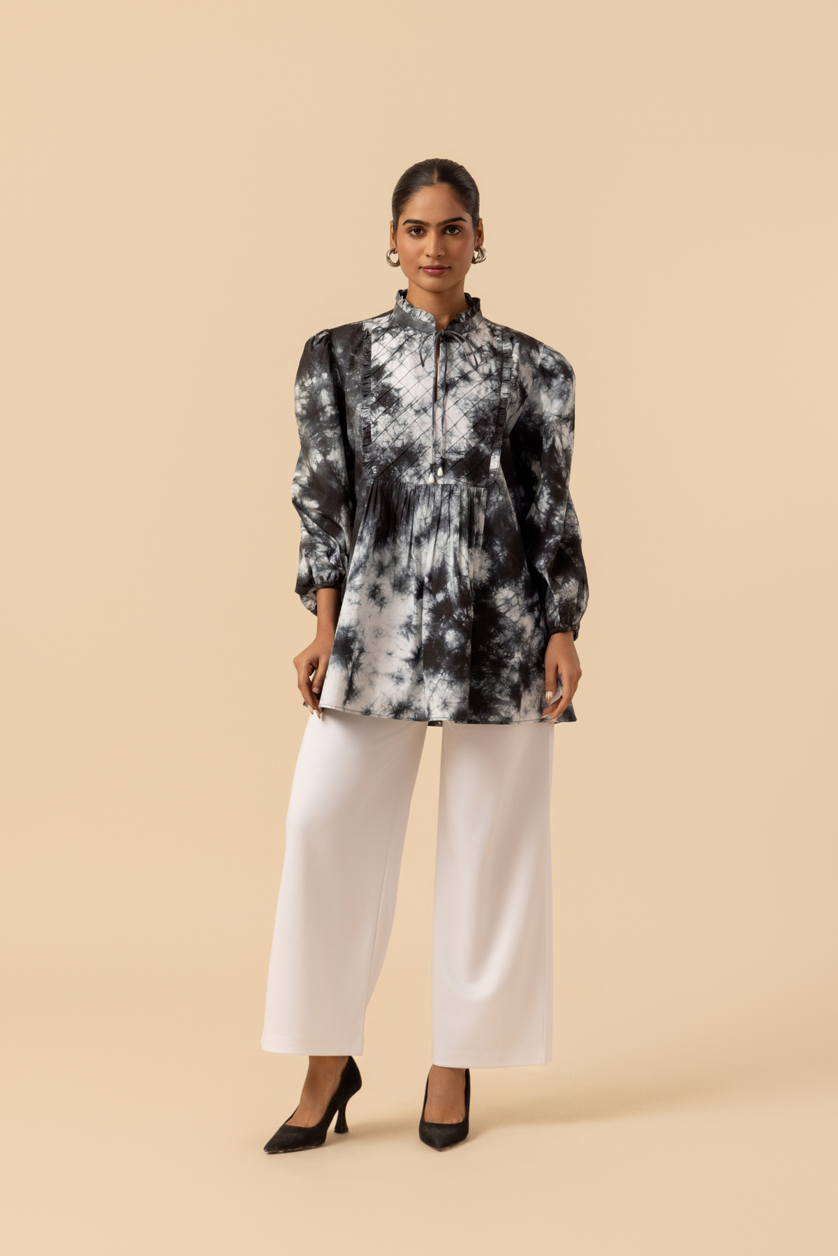 A model wears a vibrant black & white tie-dye shirt dress with puffed sleeves, paired with white wide-leg trousers and stylish sandals.