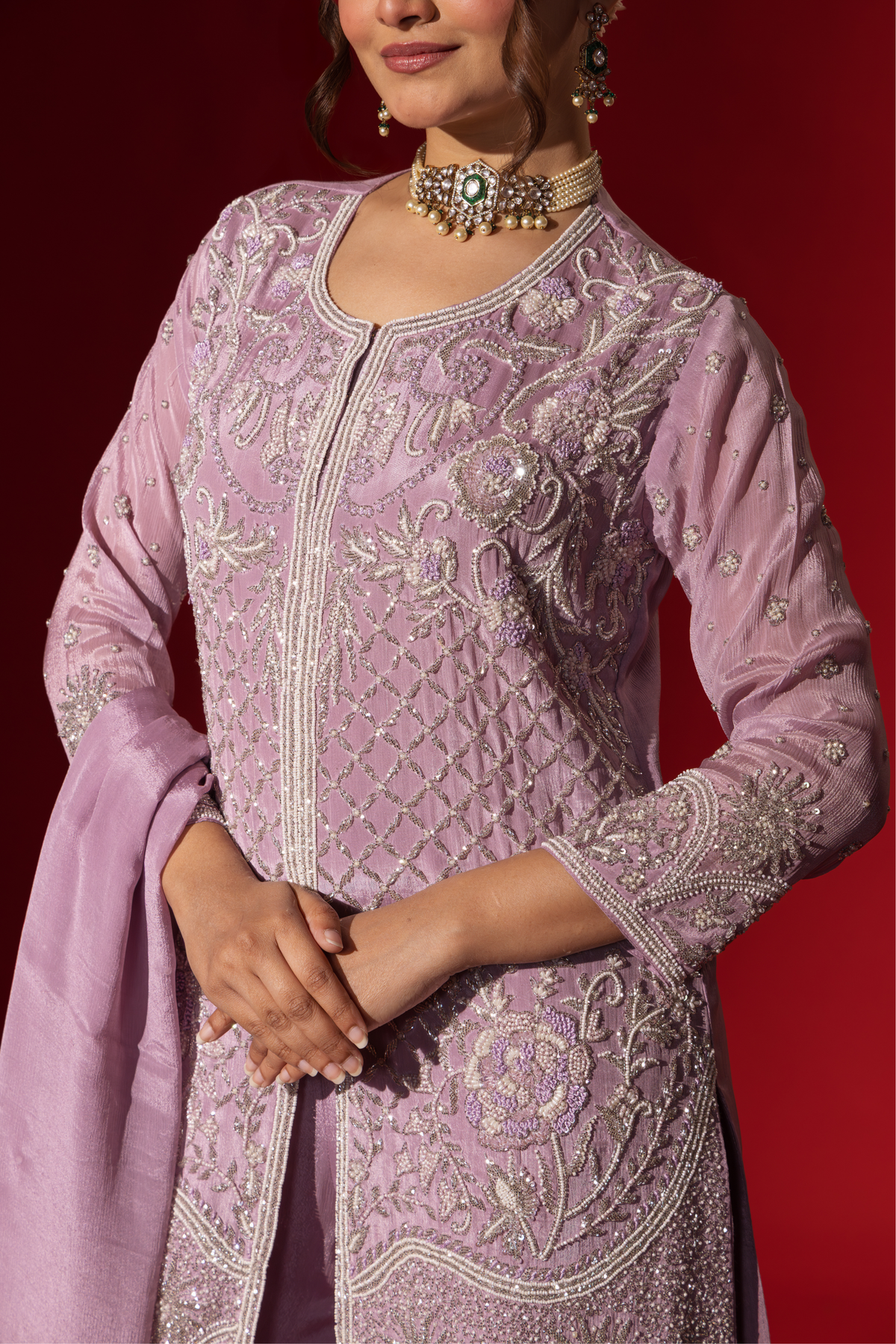 Closeup view of a woman's hand confidently in a beautifully lavender embroidered kurta set, against a rich red background.