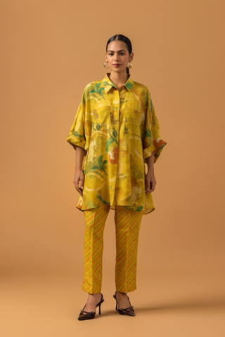 A model stands in a bright yellow co-ord set featuring a patterned oversized shirt and matching striped pants against a warm backdrop.