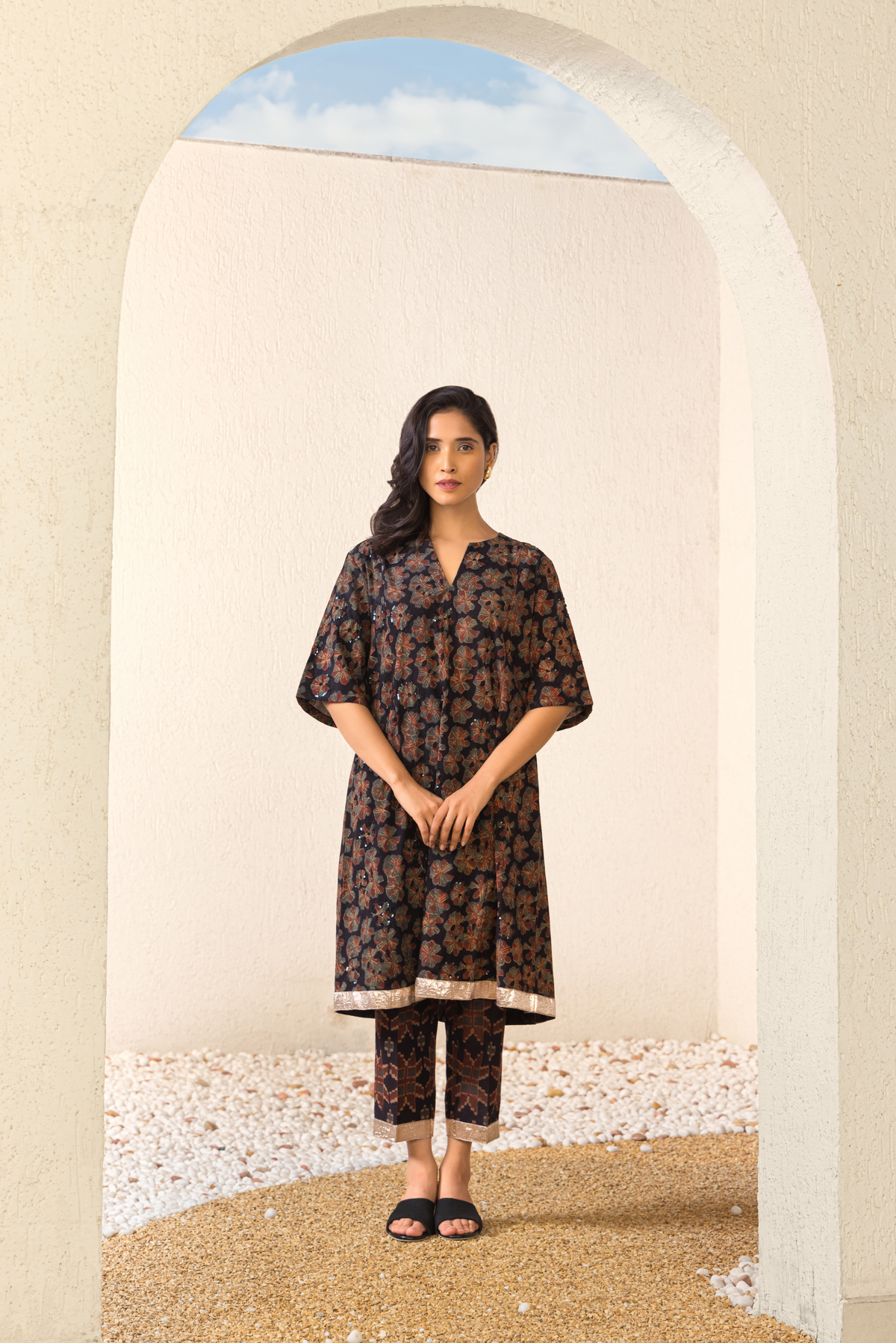 Model wearing a black floral linen kurta set with matching pants, styled in an elegant outdoor archway setting.