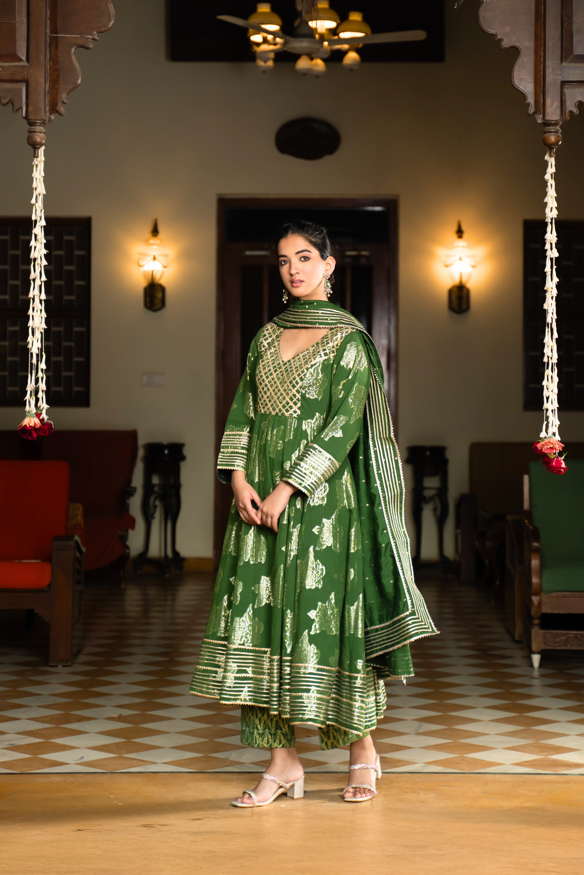Side view of a woman in a vibrant green anarkali kurta set with matching pants stands gracefully in a well-decorated interior.