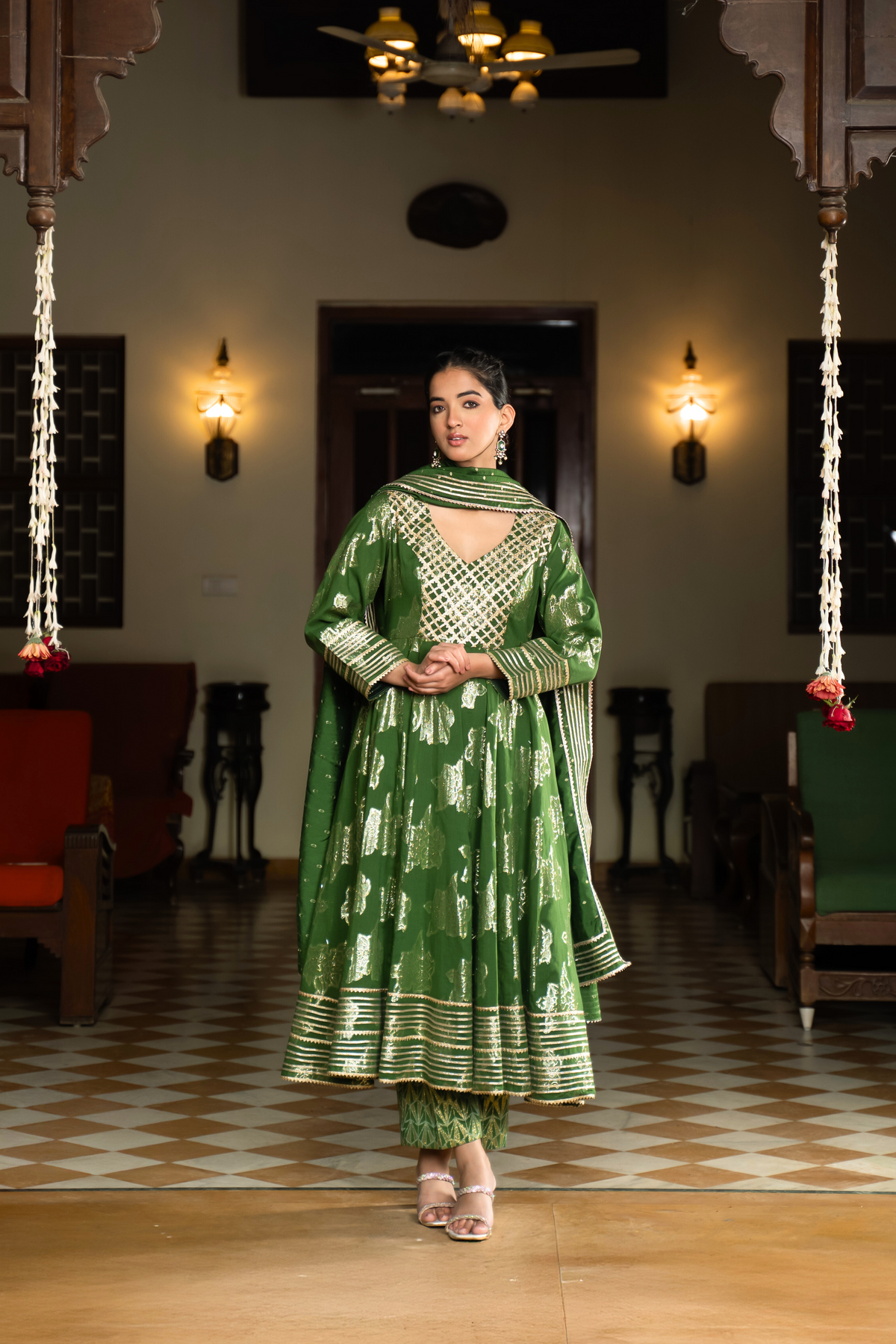 A woman in a vibrant green anarkali kurta set with matching pants stands gracefully in a well-decorated interior.