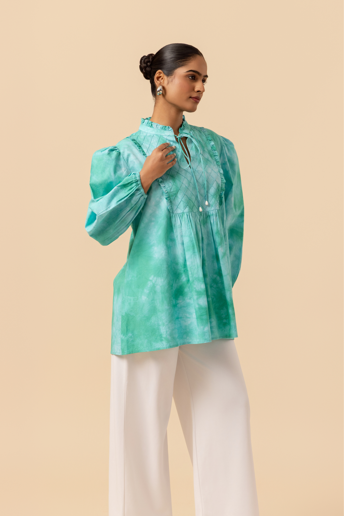 Right side view of a model wears a vibrant ocean mist tie-dye shirt dress with puffed sleeves, paired with white wide-leg trousers and stylish sandals.