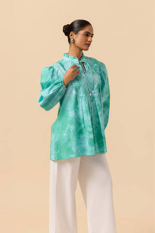 Right side view of a model wears a vibrant ocean mist tie-dye shirt dress with puffed sleeves, paired with white wide-leg trousers and stylish sandals.