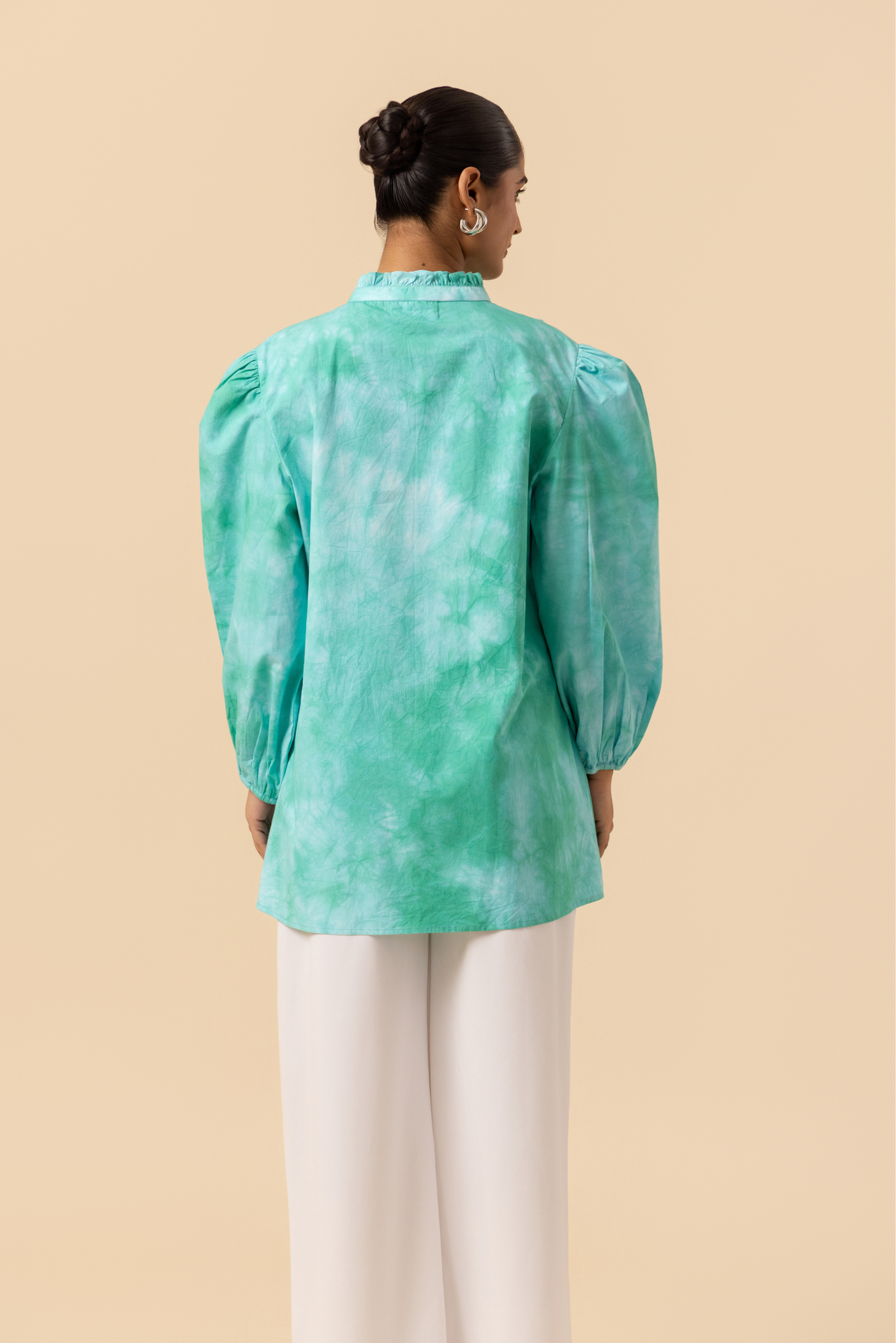 Back view of a model wears a vibrant ocean mist tie-dye shirt dress with puffed sleeves, paired with white wide-leg trousers and stylish sandals.