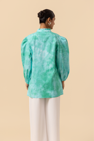 Back view of a model wears a vibrant ocean mist tie-dye shirt dress with puffed sleeves, paired with white wide-leg trousers and stylish sandals.