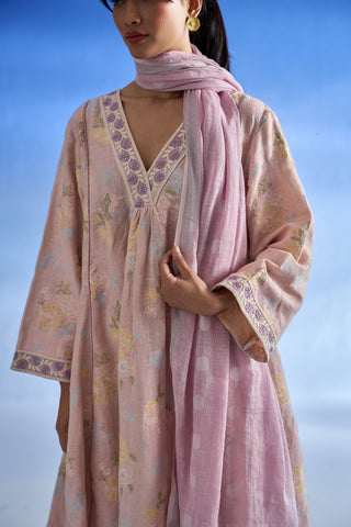 Closeup view of a woman wearing a light pink linen kurta set with floral embroidery and a matching scarf, set against a soft blue sky background.