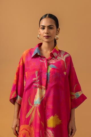 Closeup view of a model in a vibrant pink tunic with floral patterns co-ord set, paired with striped pink pants and stylish heels, against a warm, neutral background.