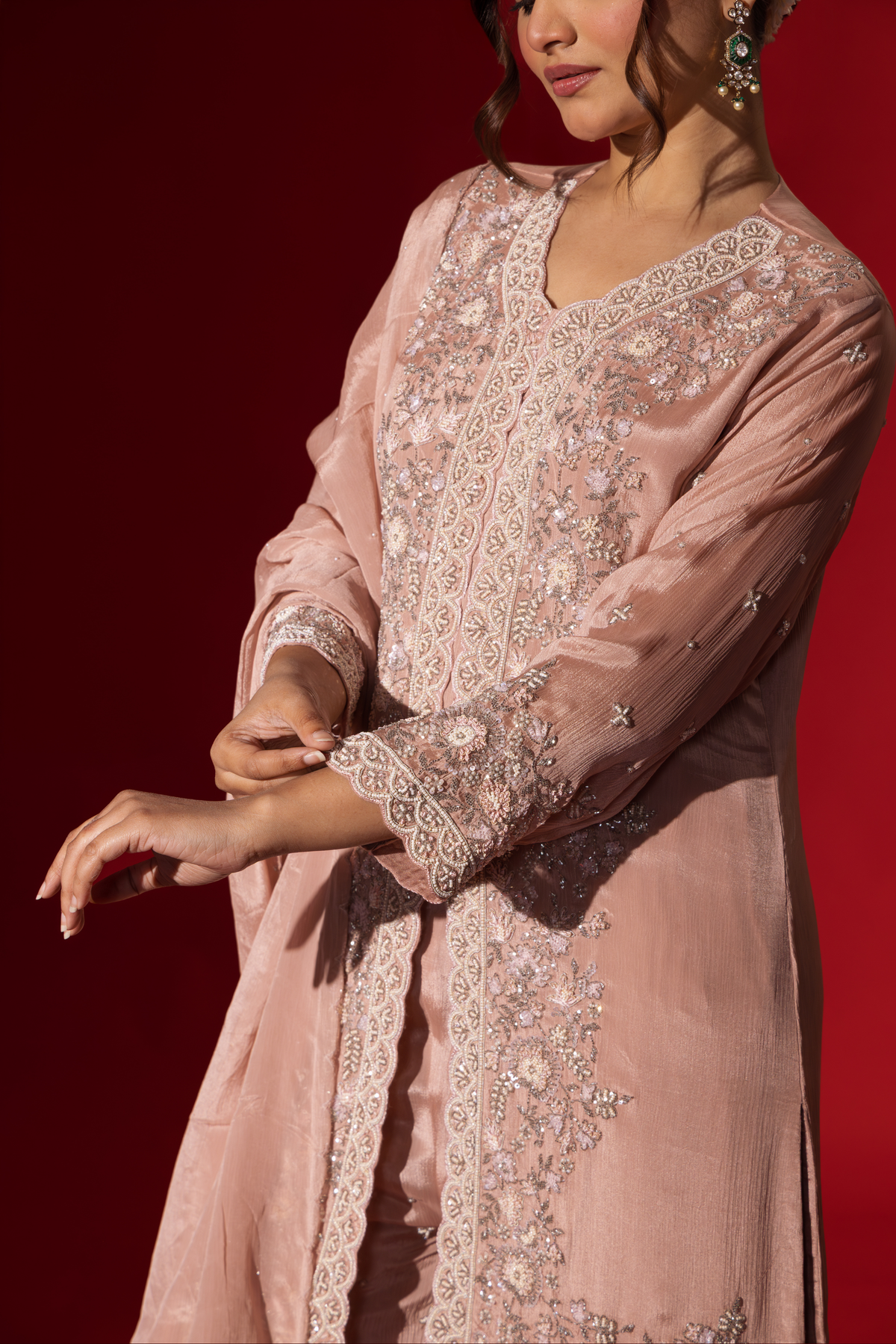 Closeup view of a woman's hand wears an elegant pastel pink embroidered kurta set with intricate beadwork, standing against a vibrant red background.