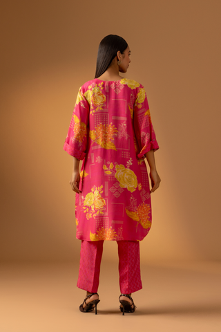 Back view of a model showcases a vibrant pink floral co-ord set with matching pants, set against a warm neutral background. 