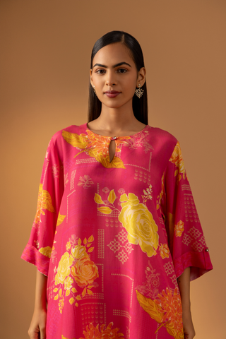 Closeup view of a model showcases a vibrant pink floral co-ord set with matching pants, set against a warm neutral background. 
