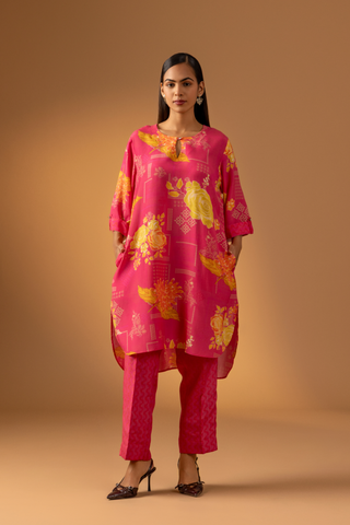 A model showcases a vibrant pink floral co-ord set with matching pants, set against a warm neutral background. 