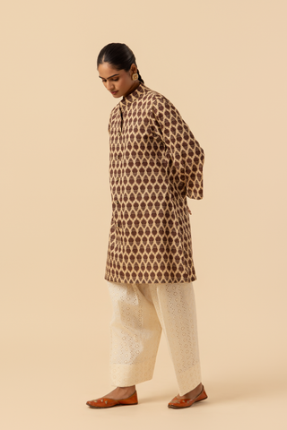 Side view of a person wearing a traditional brown patterned chikan farshi salwar co-ord set with white embroidered pants and brown sandals, set against a neutral background.