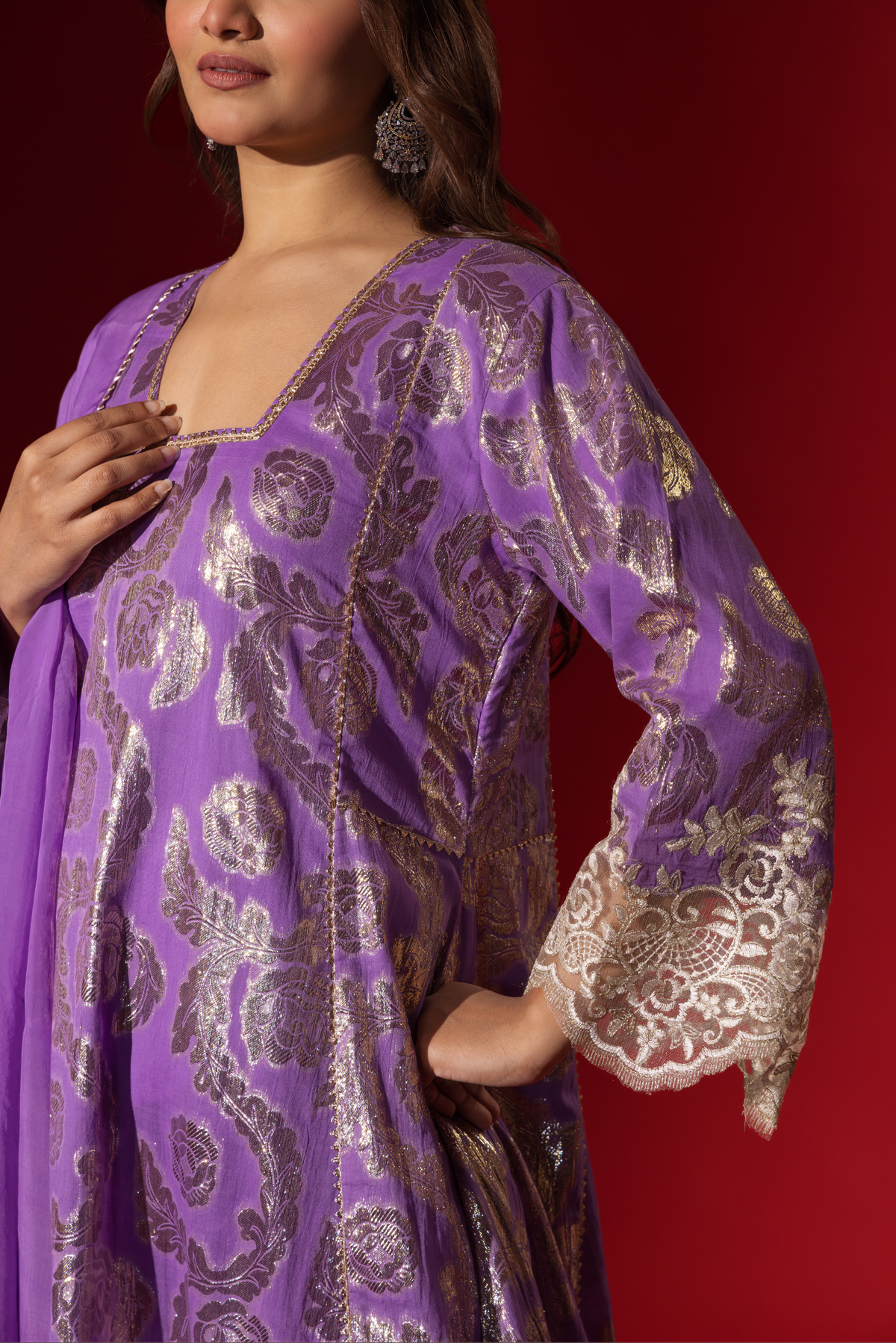 Cloaseup view of a woman's hand in a purple ethnic  shimmer kurta set outfit with intricate white embroidery against a vibrant red backdrop.