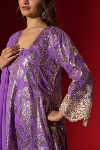 Cloaseup view of a woman's hand in a purple ethnic  shimmer kurta set outfit with intricate white embroidery against a vibrant red backdrop.