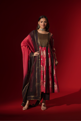 A model poses in a vibrant red and black traditional outfit, adorned with intricate patterns and complemented by elegant jewelry.