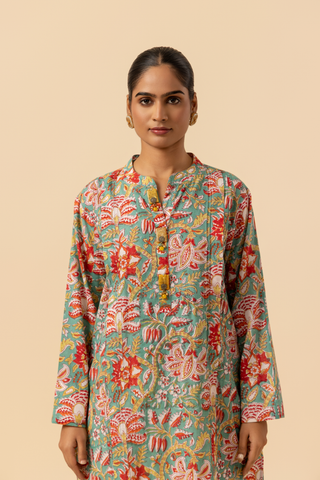 Closeup view of a person stands elegantly in a colorful floral co-ord set paired with white embellished pants and traditional sandals against a soft beige background.