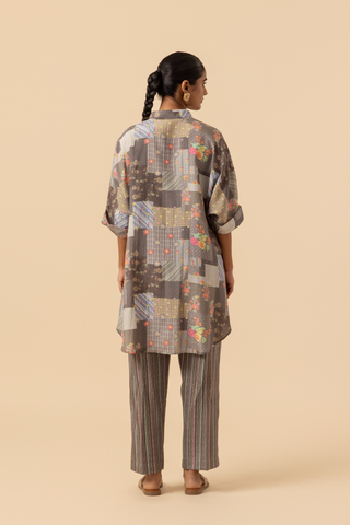 Back view of a woman wearing a floral patterned oversized shirt and striped pants, standing against a neutral background.