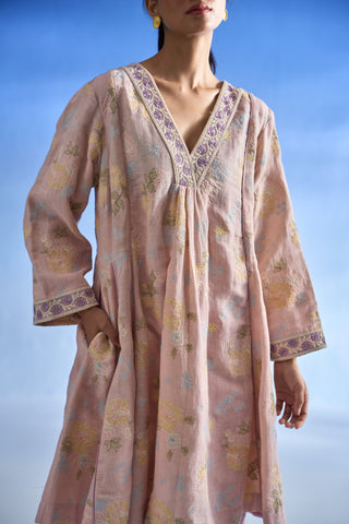 Closeup view of a woman wearing a light pink cotton  linen kurta set with yellow and purple floral prints and embroidered trim, set against a blue sky background.