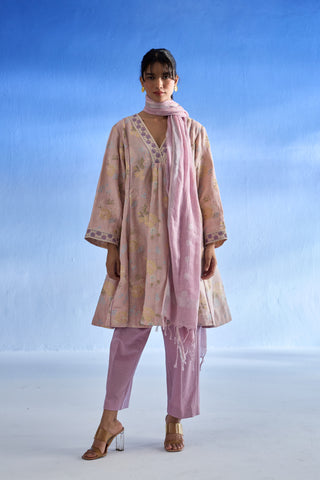 A woman modeling a light pink printed linen kurta set with matching trousers and a dupatta against a blue gradient studio background.