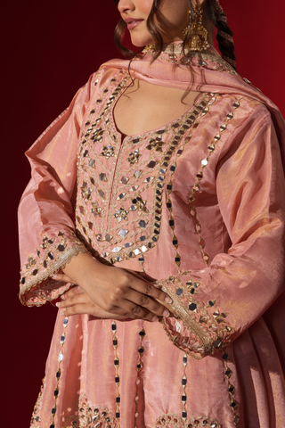 Closeup view of a  woman's hand in a rose embroidered kurta set with intricate patterns, complemented by a matching dupatta against a bold red background.