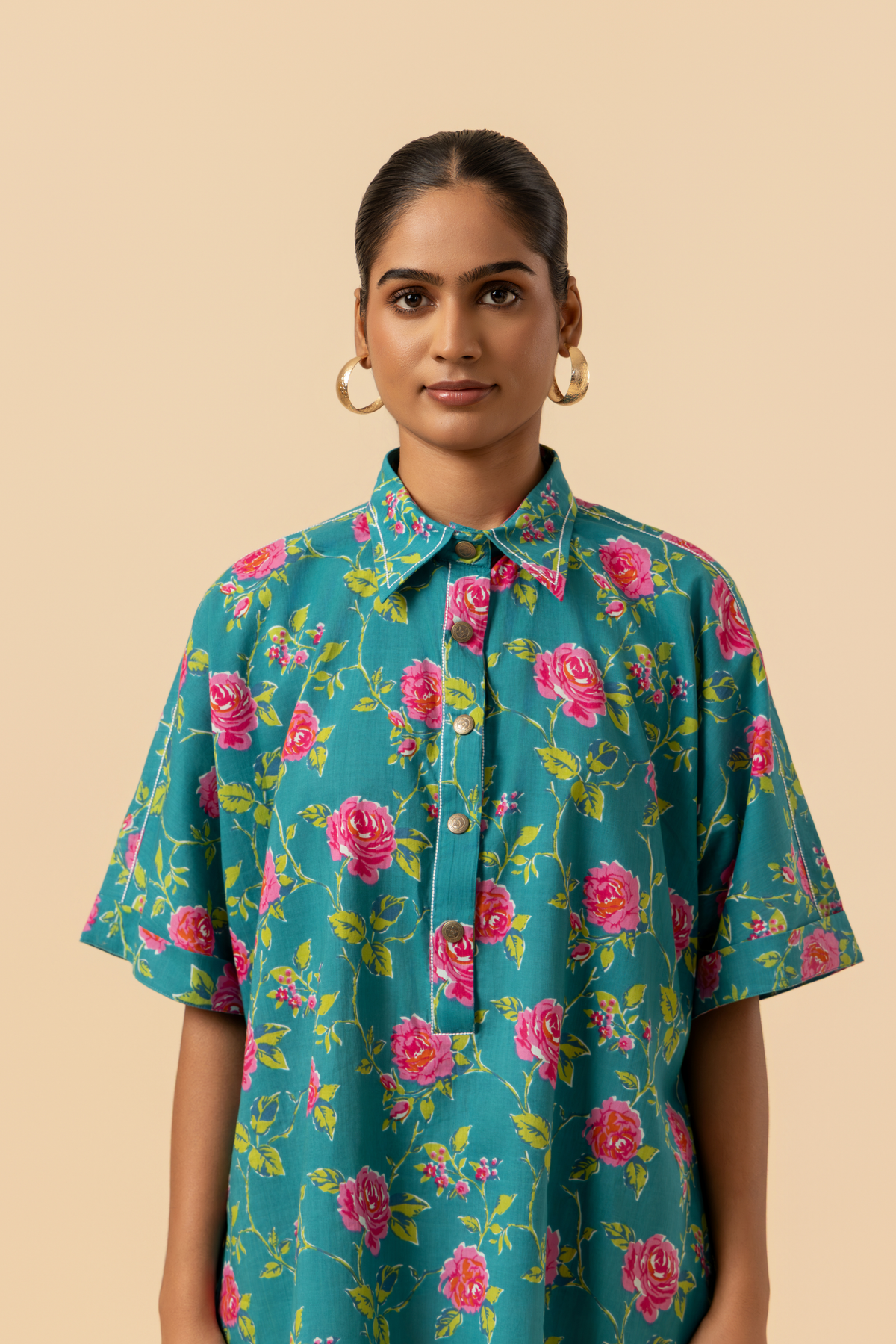 Closeup view of a person models a vibrant floral outfit, featuring a teal shirt and matching pants adorned with pink roses, set against a neutral background.