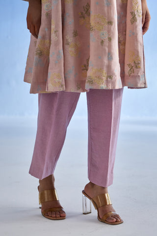 A person wearing a rose bloom floral printed linen kurta set, dusty purple straight-leg trousers, and gold heeled sandals against a pale blue studio background.