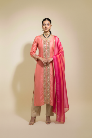 A woman wears a traditional pink tissue chanderi kurta set adorned with intricate embellishments, paired with a light pink dupatta and beige trousers.