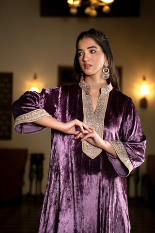 Closeup view of  a woman stands confidently in a traditional purple velvet co- ord set outfit with intricate embroidery, set against a classic interior with warm lighting.