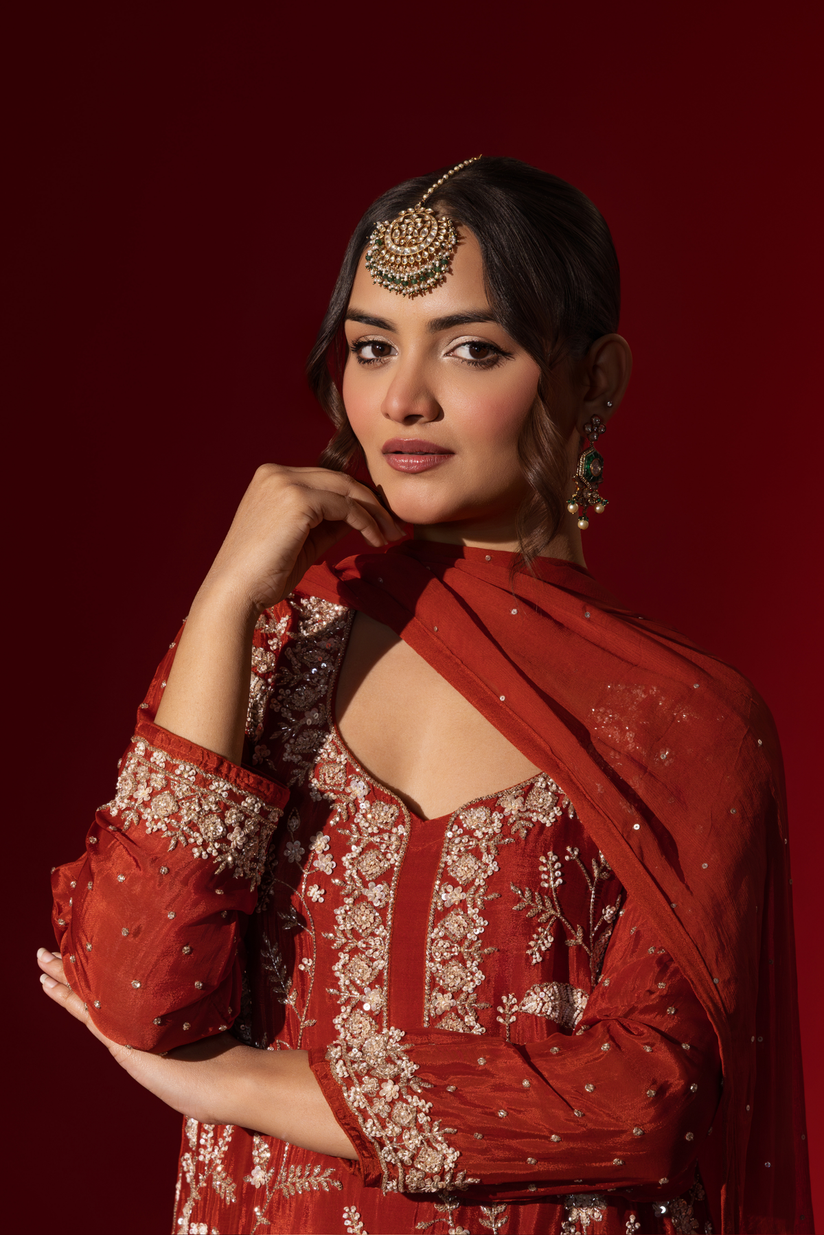 Closeup view of a woman poses in an elegant red embroidered kurta set adorned with intricate white embroidery against a rich red background.