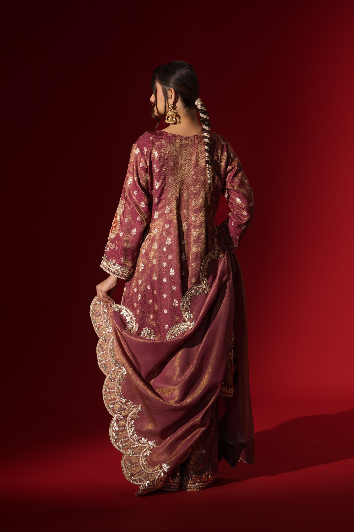 Back view of a woman wearing a richly embellished maroon embroidered brocade kurta set outfit with intricate gold detailing against a striking red background.