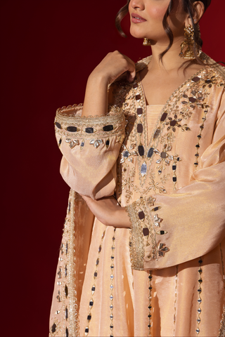 Closeup view of a woman's hand in a beige embroidered kurta set with intricate patterns, complemented by a matching dupatta against a bold red background.