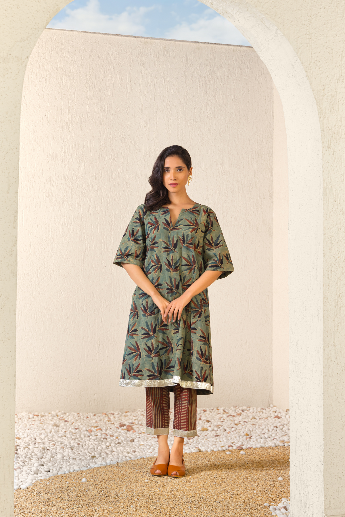 Model wearing a green botanical print linen kurta set with matching pants, styled in a minimalist outdoor archway setting.