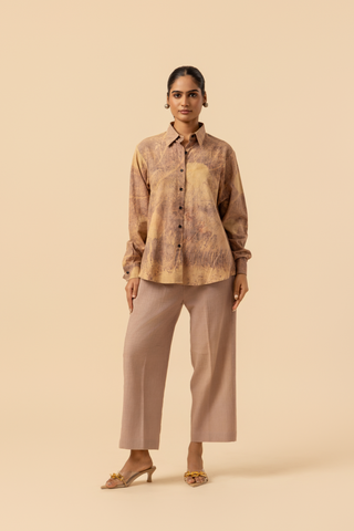 A model stands against a light beige background, wearing a patterned co-ord set which has button-up shirt and wide-legged beige pants, accessorized with heels.