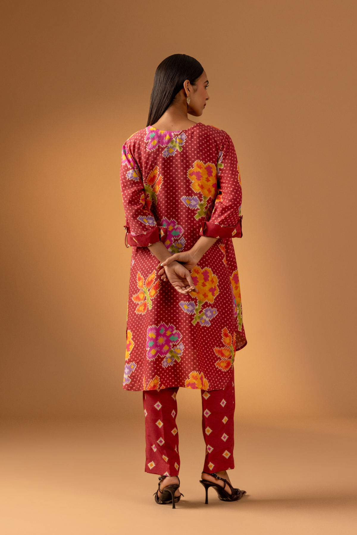 Back view of a model wears a vibrant floral co-ord set over matching patterned pants, set against a warm, neutral backdrop.