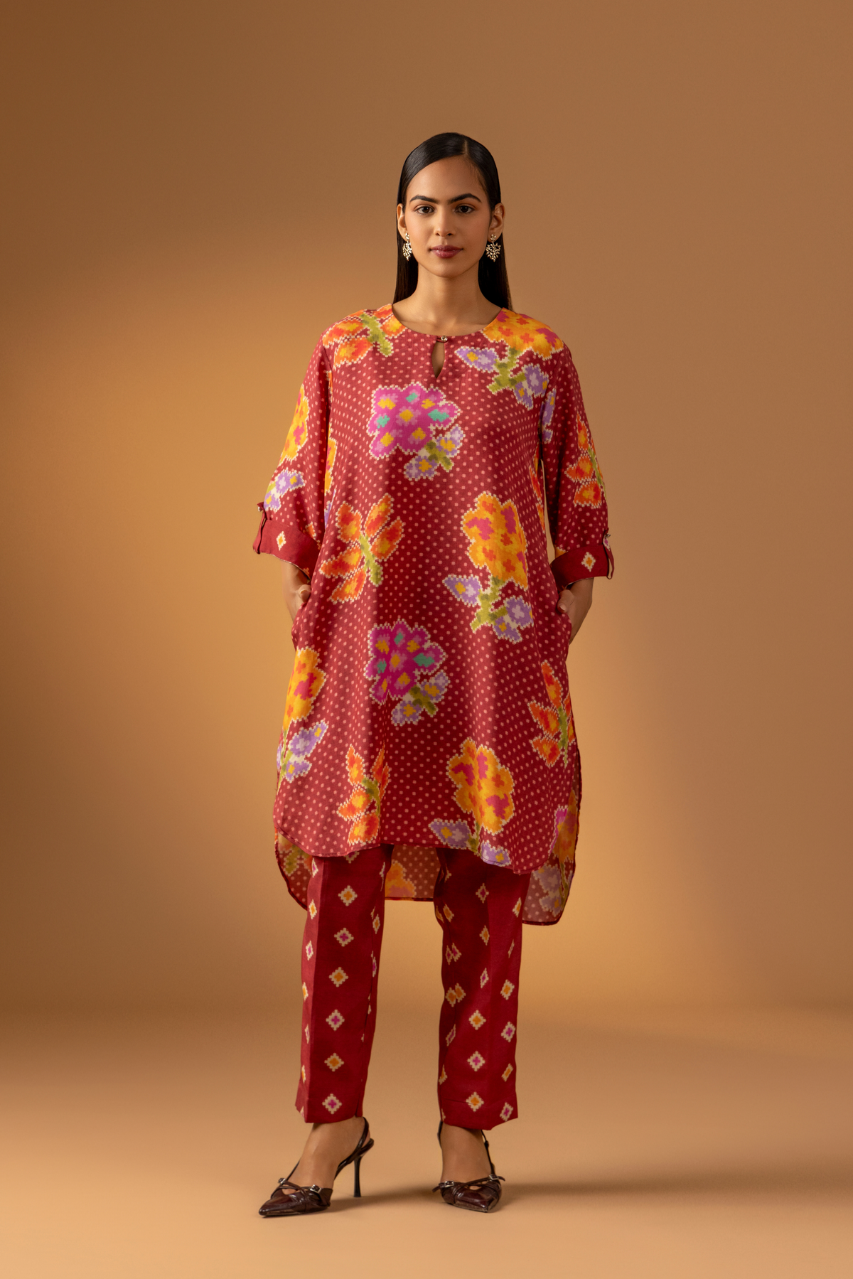 A model wears a vibrant floral co-ord set over matching patterned pants, set against a warm, neutral backdrop.