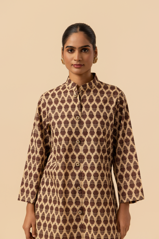 Closeup view of a view of a person wearing a traditional brown patterned chikan farshi salwar co-ord set with white embroidered pants and brown sandals, set against a neutral background.