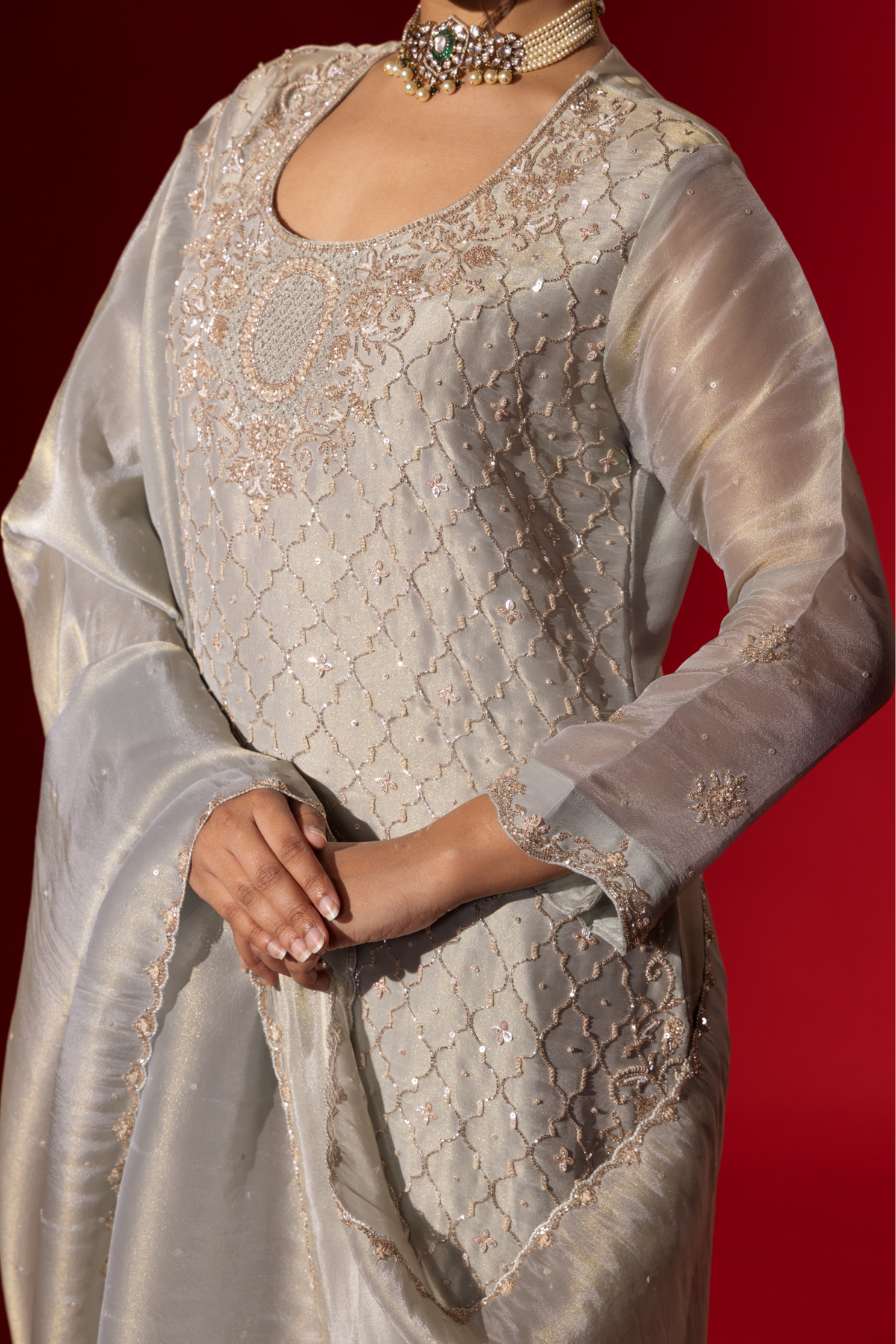 Closeup view of a woman's hand elegantly in a shimmering silver grey embroidered gharara set, featuring intricate embroidery, paired with matching wide-legged trousers and a flowing shawl.