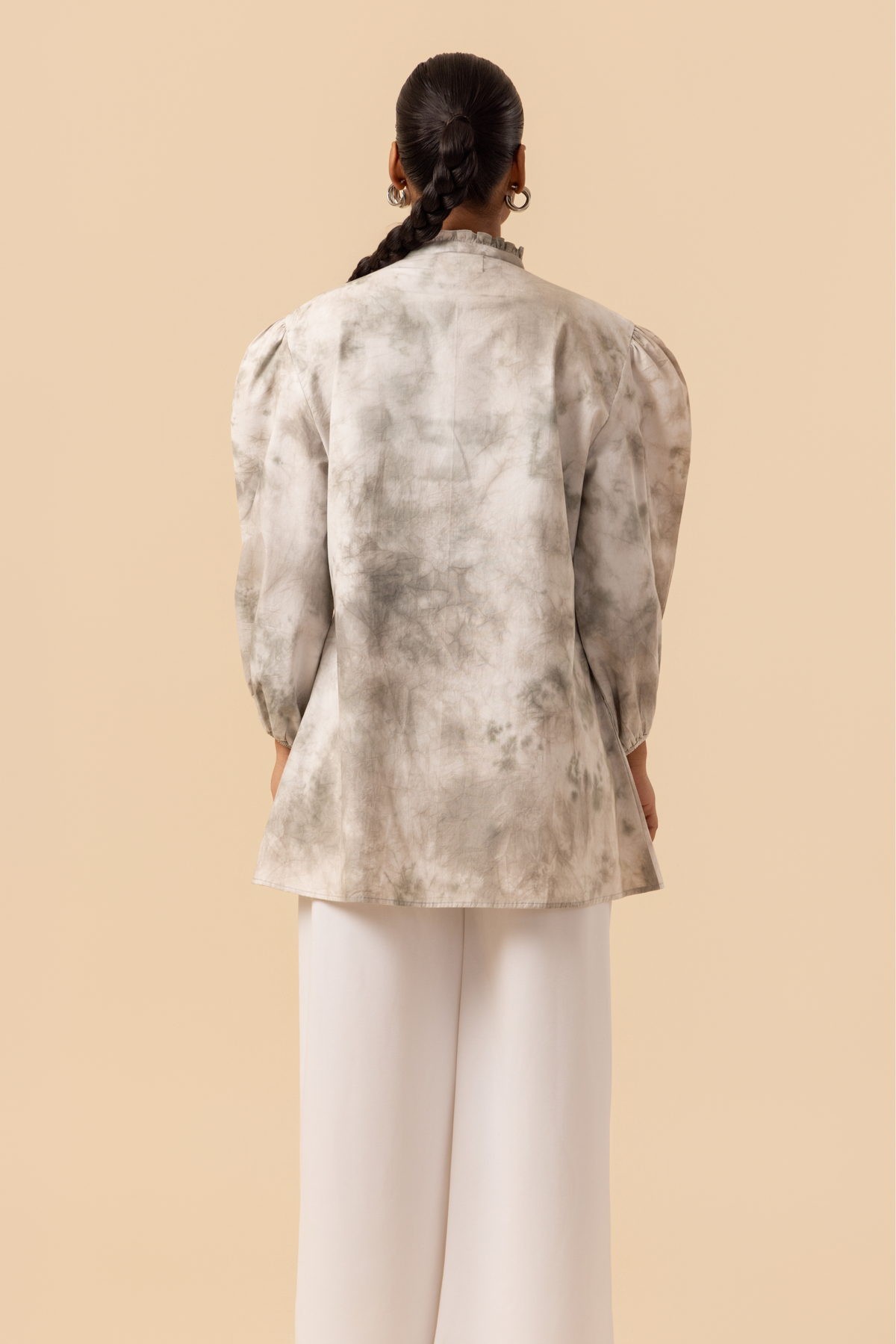Back side view of a model wears a vibrant white & grey tie-dye shirt dress with puffed sleeves, paired with white wide-leg trousers and stylish sandals.