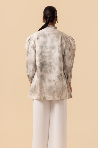 Back side view of a model wears a vibrant white & grey tie-dye shirt dress with puffed sleeves, paired with white wide-leg trousers and stylish sandals.