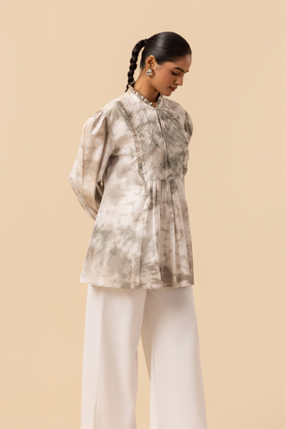 Right side view of a model wears a vibrant white & grey tie-dye shirt dress with puffed sleeves, paired with white wide-leg trousers and stylish sandals.