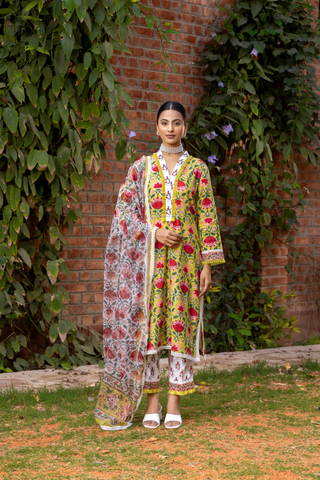 A person wears a vibrant turquoise and yellow handblock printed kurta set, standing gracefully on a checkered floor amidst lush greenery.