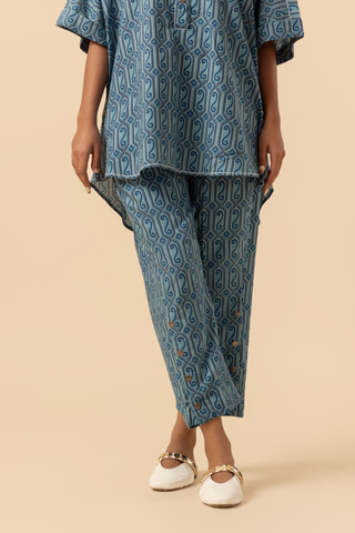 A person stands in a patterned blue matching outfit stands confidently against a neutral background, set against a soft beige background against a neutral backdrop.