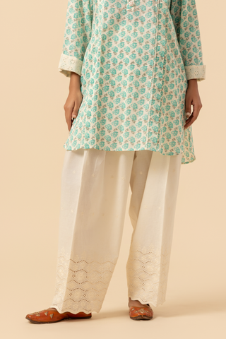A person stands wearing a light teal & white cotton farshi salwar co-ord set, set against a soft beige background against a neutral backdrop.