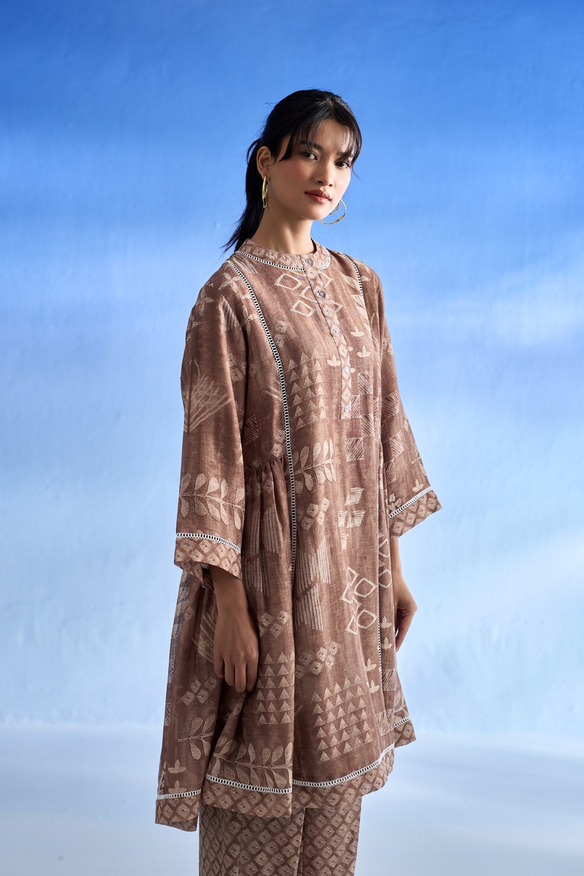 Left side view of woman wearing a brown patterned co-ord set against a blue sky.
