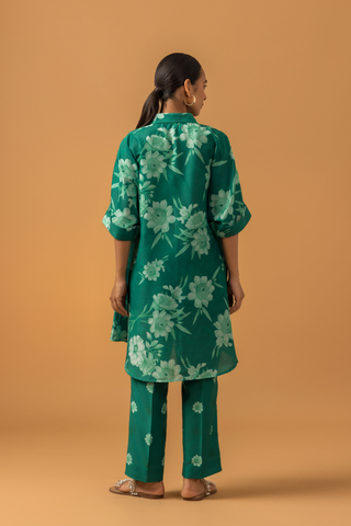 Back view of a model poses in a vibrant green floral co-ord set, featuring a loose shirt and matching pants, complemented by embellished sandals.