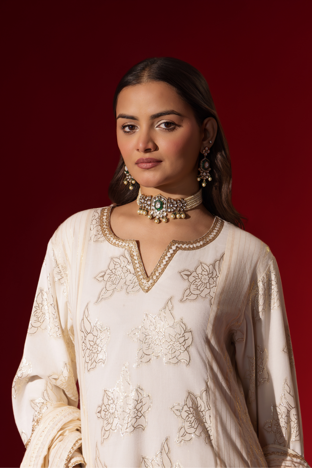 Closeup view of a woman showcases an elegant white anarkali kurta set with intricate designs, contrasting beautifully against a deep red background.